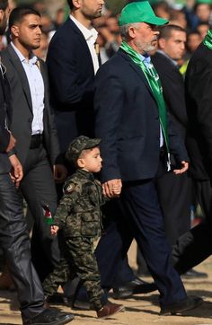 an older man in a suit and tie walking with a young boy wearing a green hat