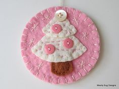 a pink and white ornament with a button on it's side that has a christmas tree in the center