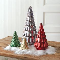 three tinsel christmas trees sitting on top of a wooden table next to each other