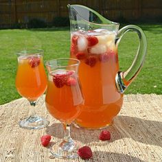 two glasses and pitcher filled with liquid sitting on a table in front of some grass