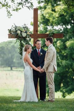 a bride and groom holding hands under a cross at their outdoor wedding in the country