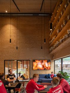 people in red shirts are sitting at tables and watching something on the wall behind them