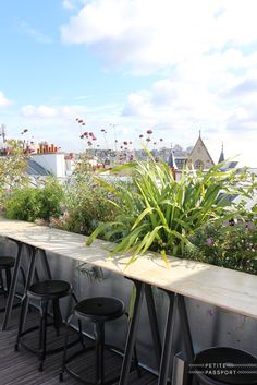 several stools and tables on a balcony with flowers in the foreground, and buildings in the background