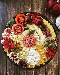 a platter filled with cheese, fruit and flowers on top of a wooden table