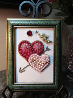 there is a framed picture with beads in the shape of a heart and an arrow