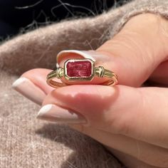 a woman's hand holding a gold ring with a red stone in the middle