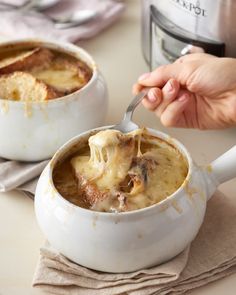 a person is holding a spoon full of food in a white bowl on a table