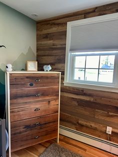 a bedroom with wood paneled walls and a dresser next to a window in the corner