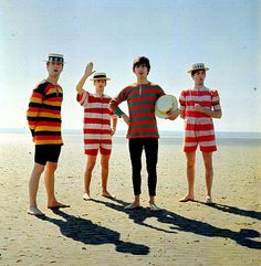 three men in striped shirts are standing on the beach and one is holding a frisbee