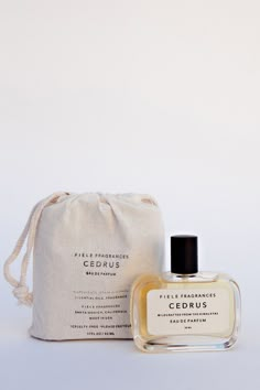 a bottle of cologne sitting next to a bag on a white surface with a drawstring