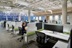 an office with cubicles, desks and people working on their laptops in the background