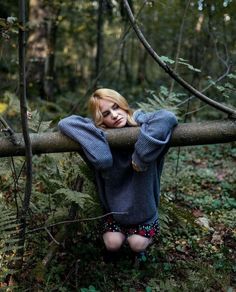 a woman is sitting on a log in the woods with her hands behind her head