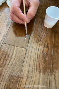 a person is holding a paintbrush and painting on wood flooring with white cups