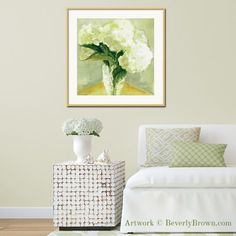 a white couch sitting in front of a painting on the wall above it is a vase with flowers