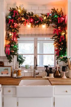 a kitchen decorated for christmas with wreaths and lights on the window sill above the sink