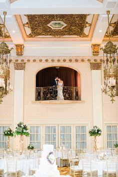 a bride and groom are standing on the balcony of their wedding reception room with chandeliers hanging from the ceiling