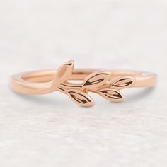 a rose gold ring with leaves on the side and a diamond in the middle, sitting on a white surface