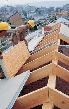 two men are working on the roof of a building that is being built with wood shingles