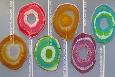 four different colored donuts hanging from strings in front of a white wall with writing on it