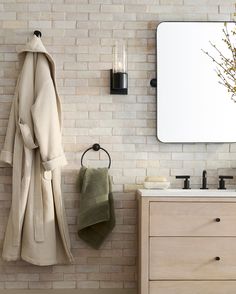 a white brick wall in a bathroom next to a wooden cabinet and sink with two towels hanging on it