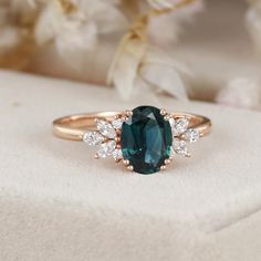 an oval cut blue and white diamond ring on top of a cushioned surface with flowers in the background