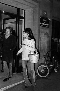 an old black and white photo of a woman walking with a basket in her hand