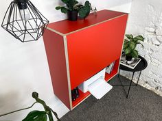 a red cabinet sitting next to a plant on top of a table