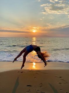 a woman is doing a handstand on the beach as the sun goes down