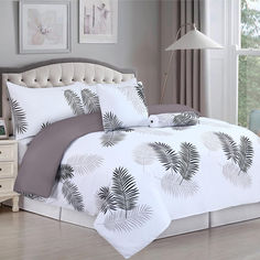 a bed with white and grey comforters in a room next to a lamp on a table