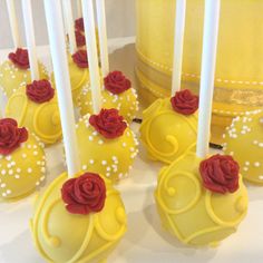 some yellow cake pops with red roses on them and white candles in front of it