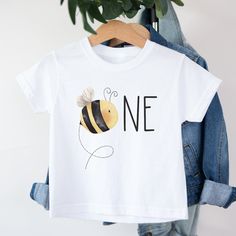 a white t - shirt with a bee on it and the words one written in black