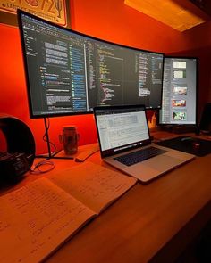 two computer monitors sitting on top of a desk next to an open notebook and keyboard