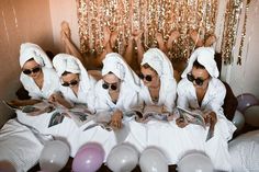 four women in bathrobes are sitting on a bed with balloons and streamers