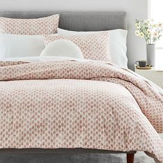 a bed with pink and white comforter in a bedroom next to a vase filled with flowers