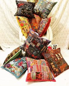 a pile of colorful pillows sitting on top of a white bed next to a curtain