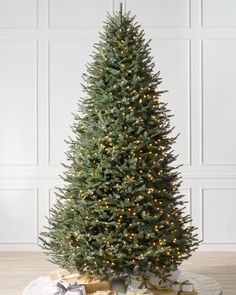 a christmas tree with presents under it on a wooden floor in front of a white wall