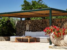 an outdoor seating area with couches and potted flowers in the foreground, surrounded by stone walls