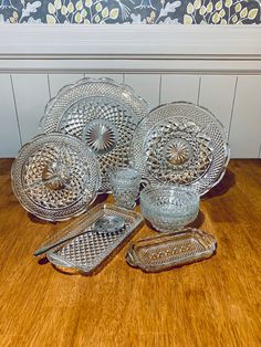 an assortment of glass dishes and trays on a wooden table with floral wallpaper