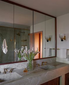 a bathroom with two sinks, mirrors and flowers in a vase on the counter top