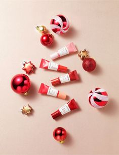 christmas ornaments and lip glosses arranged on a pink surface