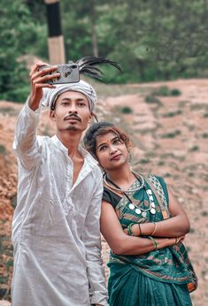 a man and woman standing next to each other in front of a dirt field with trees