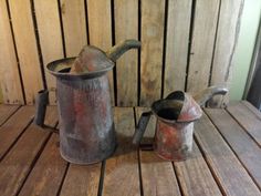 two old watering cans sitting on top of a wooden table