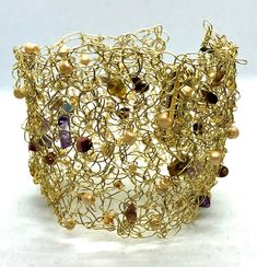 This intricately designed cuff bracelet has been crocheted with non tarnish brass wire and has a brass magnetic clasp.  Semi precious stones and glass beads have been interwoven throughout the design. This bracelet will complement any outfit and can be custom made to any size. MEASUREMENTS: Bracelet widths are: 5.5 cm, (2.16") 6 cm (2.36") and 6.5 cm (2.55"). The length of the bracelet will depend on your wrist measurement. Please measure the circumference of your wrist (not the size you want th Gold Woven Jewelry As A Gift, Gold Fusion Bracelets With Round Beads, Gold Woven Jewelry Gift, Gold Woven Jewelry For Gift, Gold Woven Bracelet Jewelry, Gold Woven Beaded Bracelets, Fusion Gold Beaded Jewelry, Fusion Style Gold Beaded Jewelry, Unique Beaded Brass Bracelets