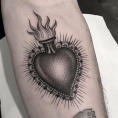 a black and white heart tattoo on the left arm with flames coming out of it