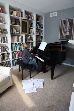 a woman sitting at a piano in front of a bookshelf filled with books