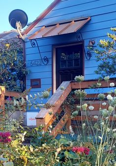 a blue house with lots of flowers in the front yard and stairs leading up to it