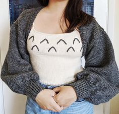 a woman standing in front of a door with her hands on her hips wearing a sweater and jeans