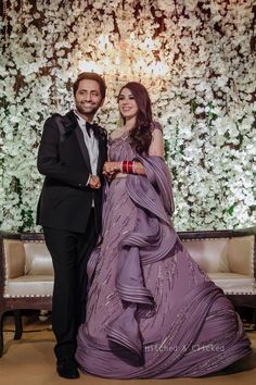 a man and woman standing next to each other in front of a flower covered wall