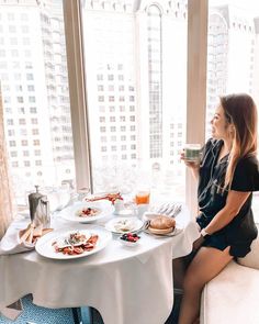 a woman sitting at a table in front of a window with breakfast foods on it