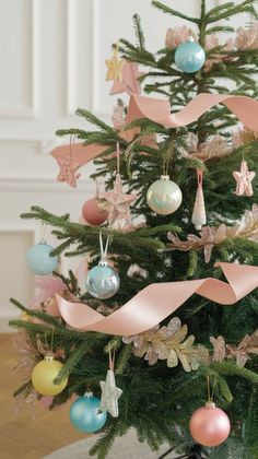 a decorated christmas tree with pink ribbon and pastel ornaments hanging from it's branches